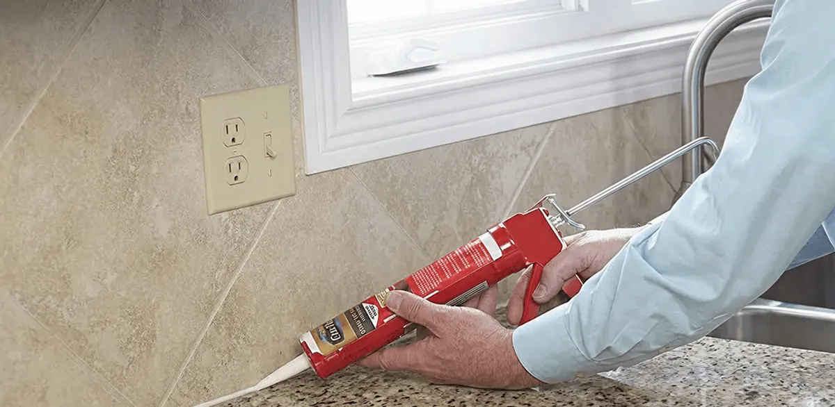 Handyman applying caulk along a kitchen backsplash and countertop seam in Baton Rouge, LA