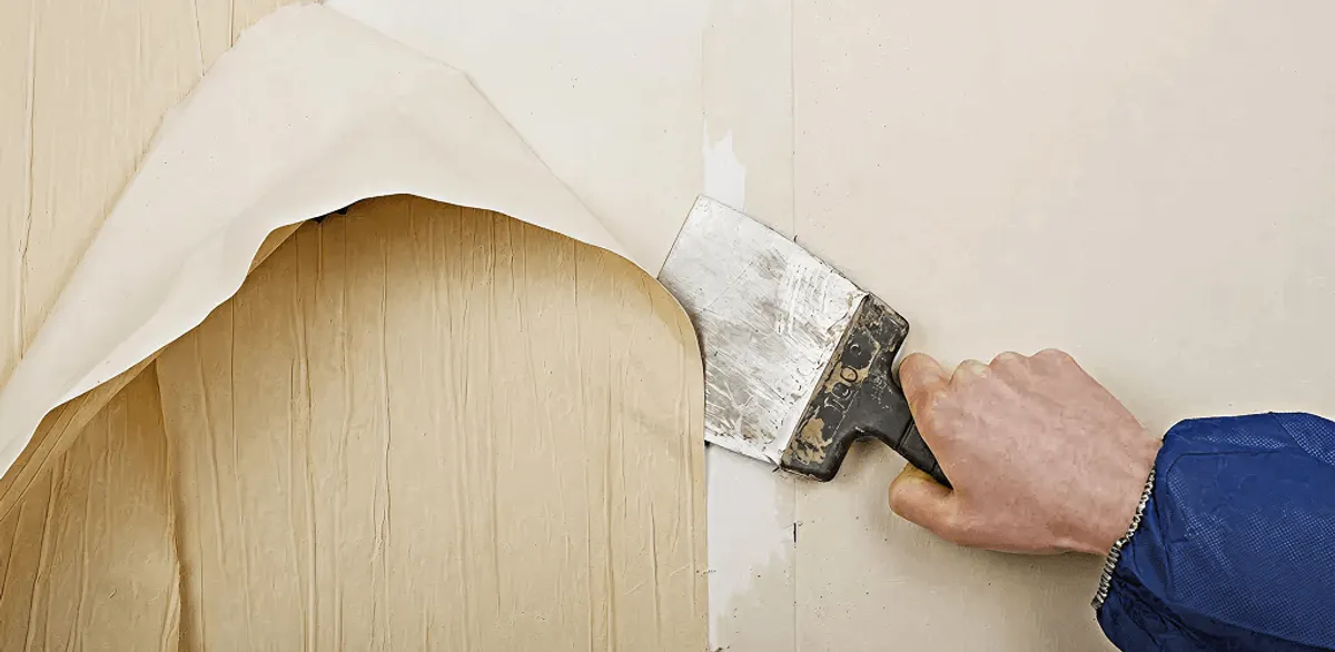 Handyman removing wallpaper with a scraper for wall preparation in Baton Rouge, LA